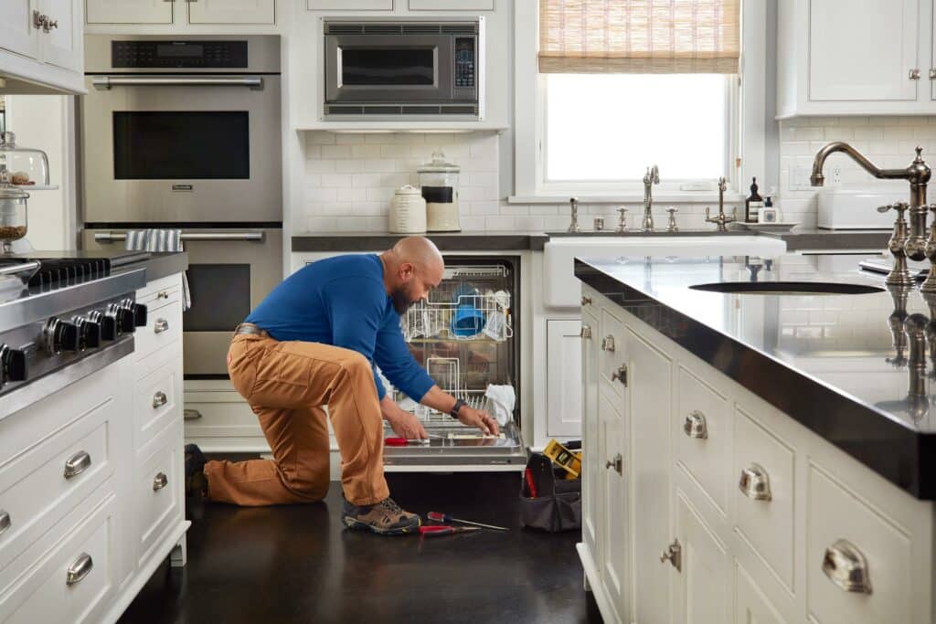 Home owner one knee on the floor fixing dishwasher - American Home Services - Home Warranties Orlando